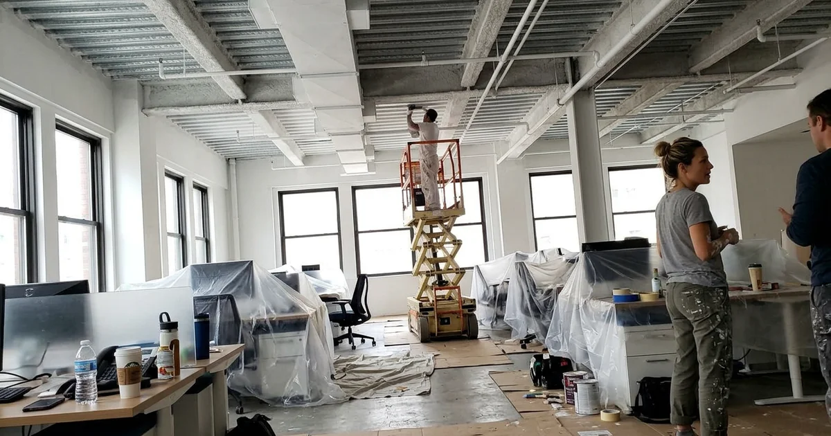 Round Rock open-plan office with a high exposed ceiling and a scissor lift set up for painting