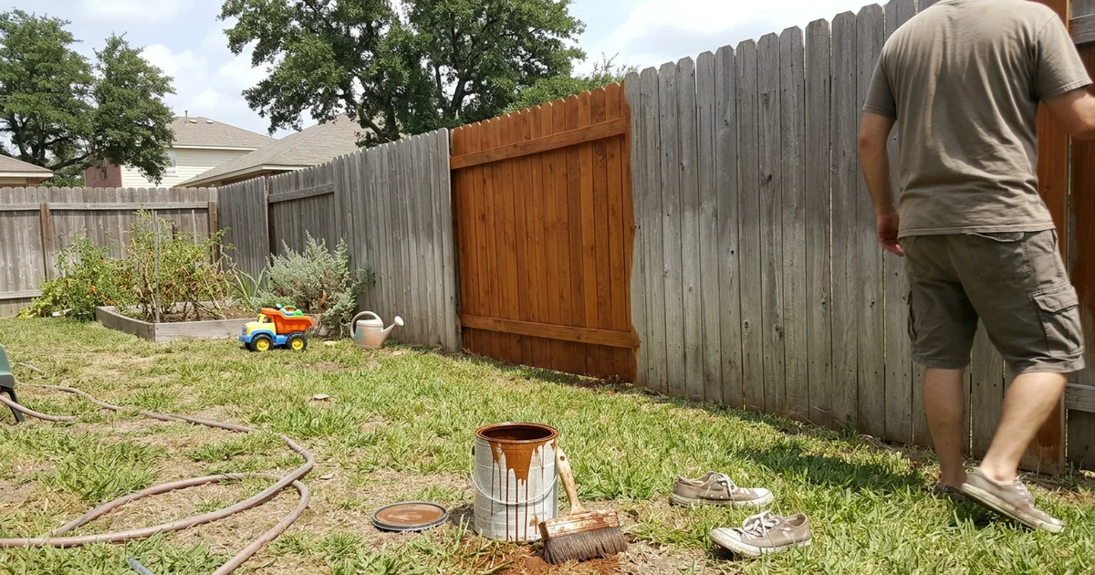 Sun-grayed cedar privacy fence in a Round Rock backyard with a half-stained section