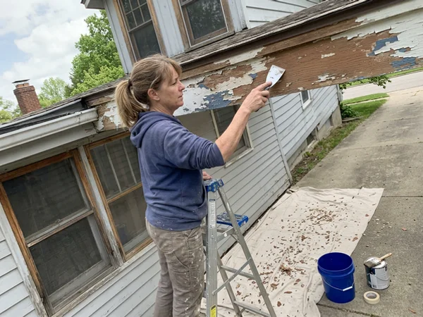 Scraping peeling paint from wood fascia on a Round Rock home before priming